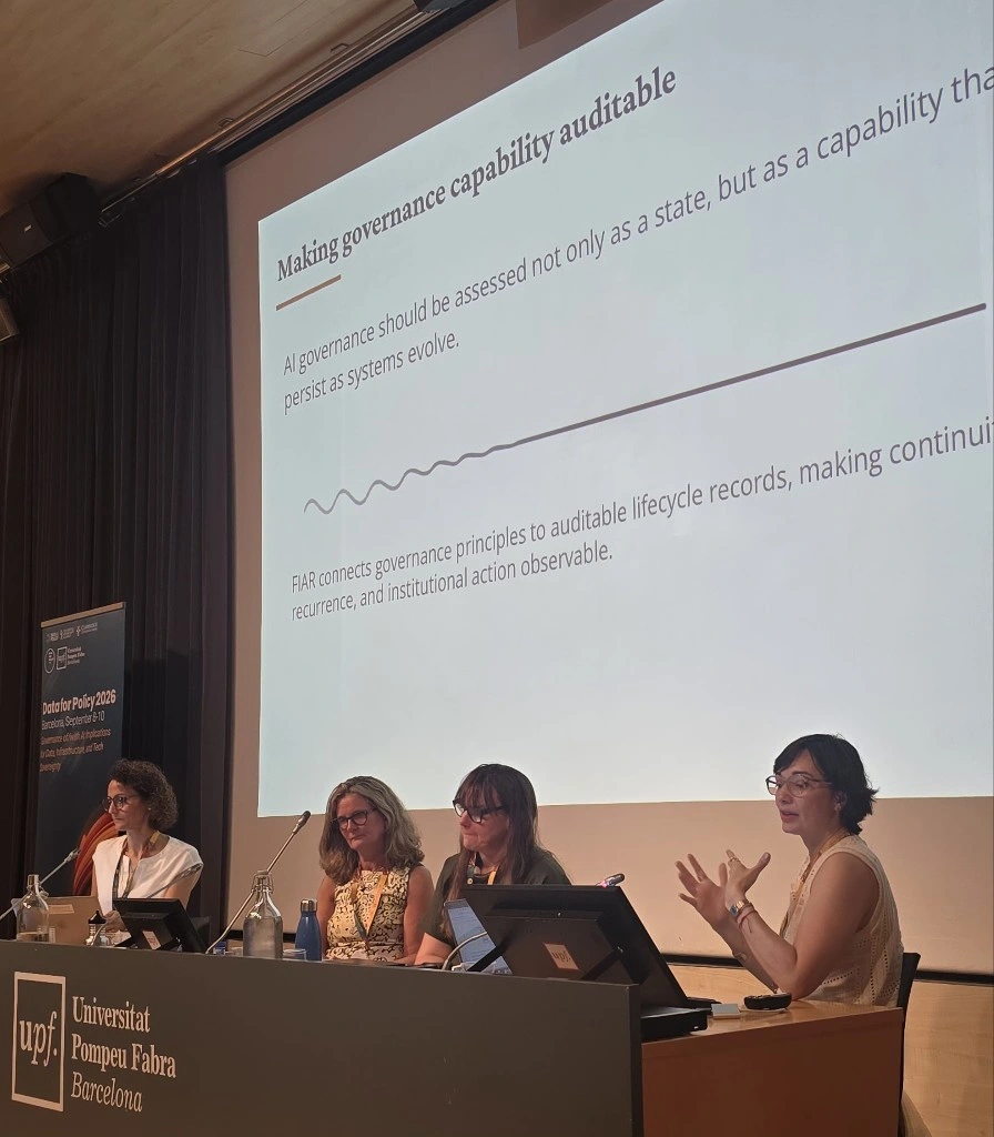 Marisa Vasconcelos apresenta o trabalho do NIAR-Saúde na Data for Policy 2026, com o slide do FIAR projetado ao fundo