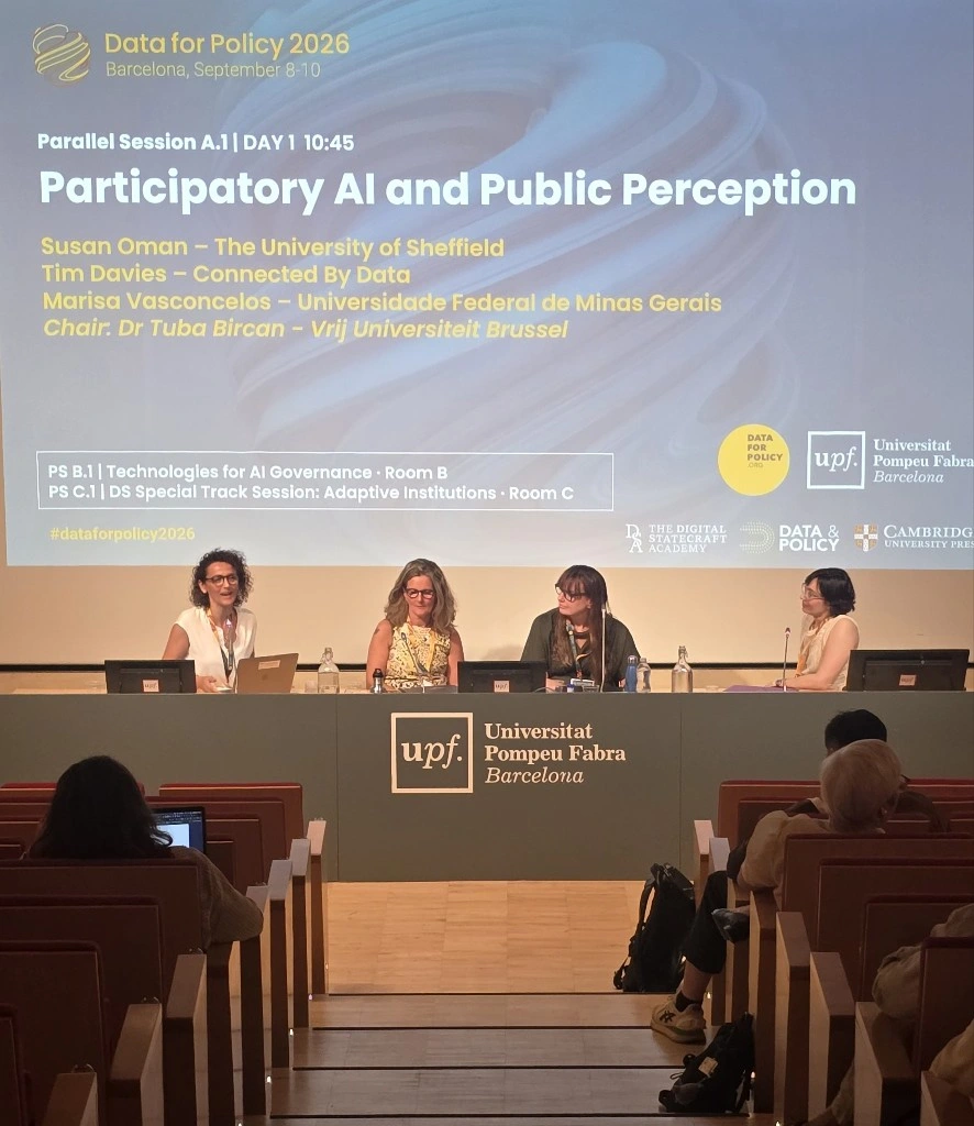 Marisa Vasconcelos apresenta o trabalho do NIAR-Saúde na Data for Policy 2026, com o slide do FIAR projetado ao fundo